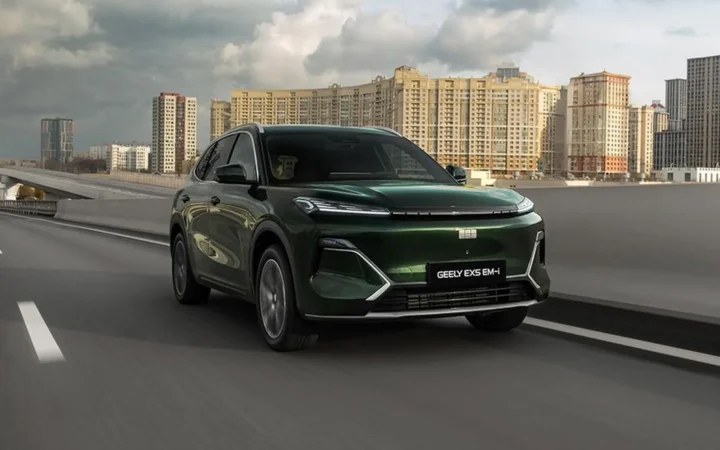 Зелёный гибридный кроссовер Geely EX5 EM-i движется по городской магистрали